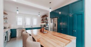 A kitchen with a large wooden island and teal cabinets.