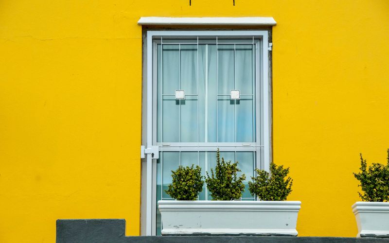 A white-framed window with security bars set against a bright yellow wall