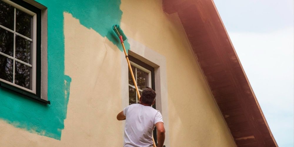 A worker paints the facade walls of a house with paint using a paint roller