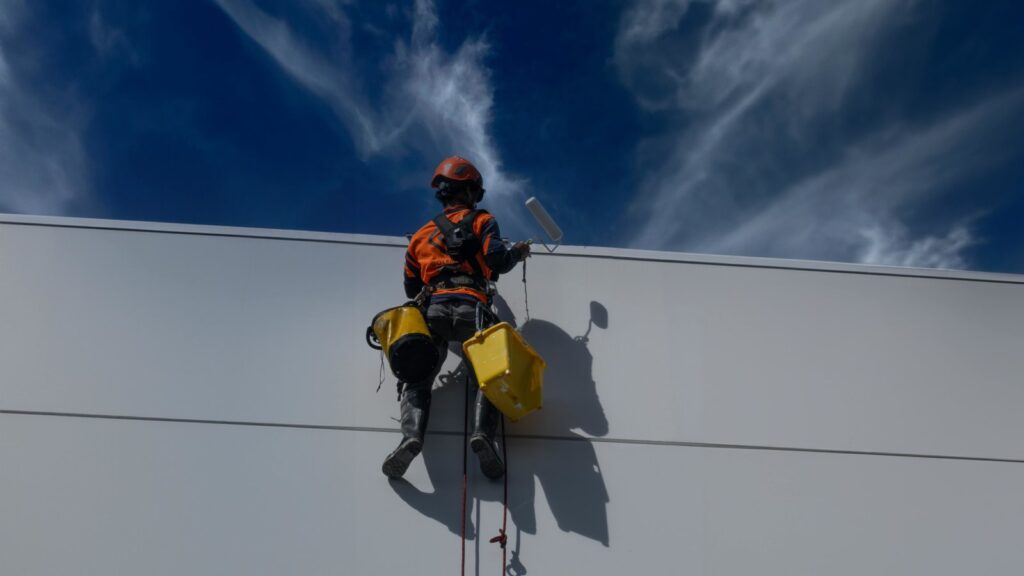 Back view of a worker painting a building wall outdoors in Auckland, New Zealand.