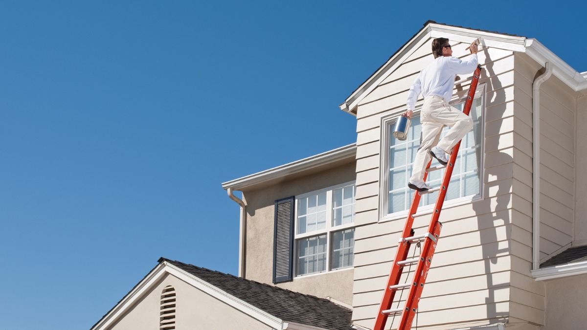 Painter holding a paint can while climbing an orange extension ladder