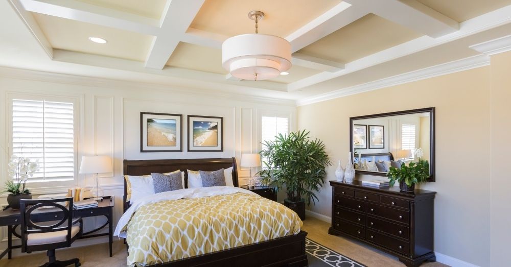 A bright, luxurious bedroom with a coffered ceiling and dark furniture.
