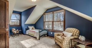 A cozy attic bedroom with blue walls and a patterned armchair.