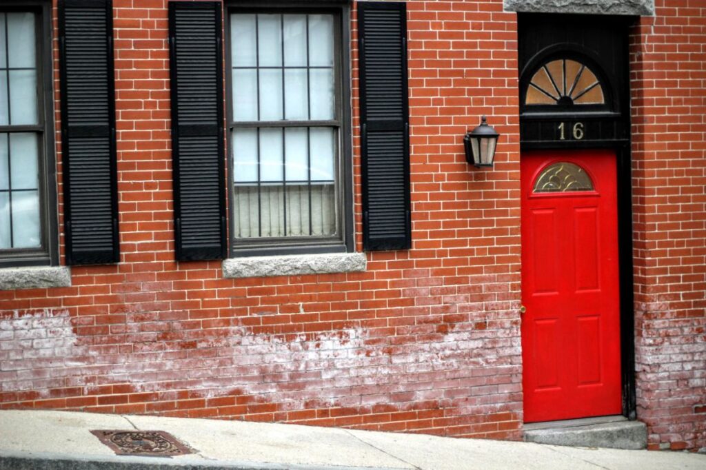 Red entrance door to a brick building showing number sixteen on a street with glass windows