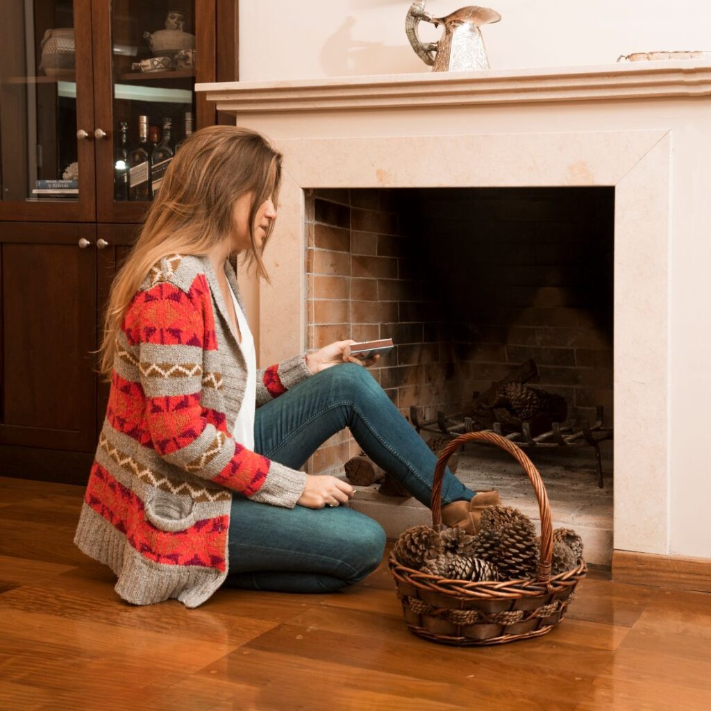 Young woman sitting outside the fireplace with matchbox and pinecone basket