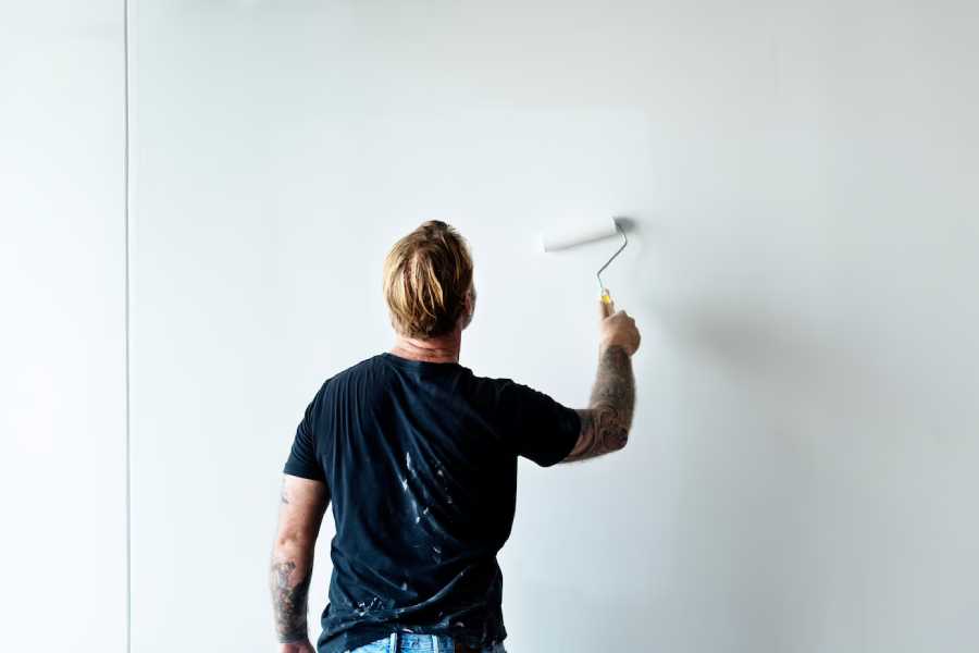A guy painting the wall white with a roller