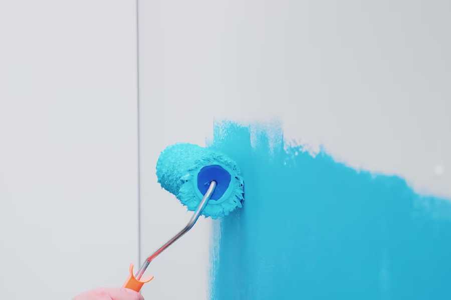 A painter painting a wall with blue paint with a roller