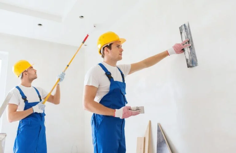 Two construction workers are working on a wall.