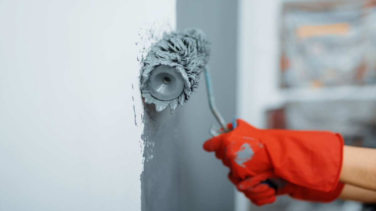 Person in red gloves using a textured roller to apply grey paint